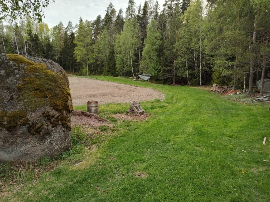 Maisema pihalta, jossa näkyy kalliota, metsän reuna ja pellon kulma.